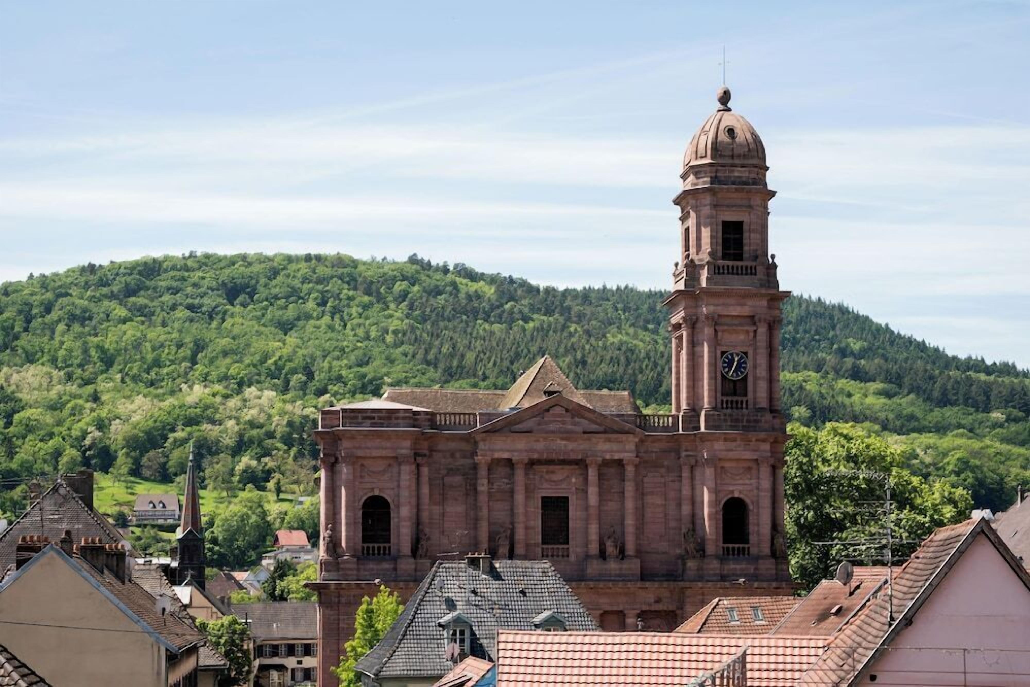 Ein historisches Gebäude mit einem markanten Glockenturm, umgeben von einer hügeligen Landschaft.