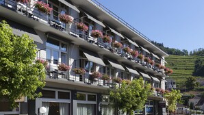 A multi-story hotel with balconies adorned with potted flowers, large windows, and a view of a hillside. - The Originals City, Hotel de L'ange, Guebwiller (Guebwiller)