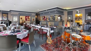 A restaurant with tables set for dining, a bar area, and a drum set in the center. - The Originals City, Hotel de L'ange, Guebwiller (Guebwiller)