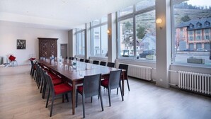 A conference room with a long table, chairs, and large windows offering a view of buildings and cars outside. - The Originals City, Hotel de L'ange, Guebwiller (Guebwiller)