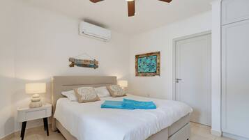 Un dormitorio con cama, mesitas de noche, ventilador de techo, aire acondicionado y una puerta.