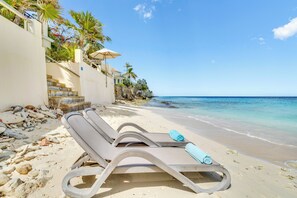 A beach with a lounge chair and umbrella, a staircase leading to a building, and a clear view of the ocean. - Oceanfront beach apartment Bellevue 2 (Kralendijk)
