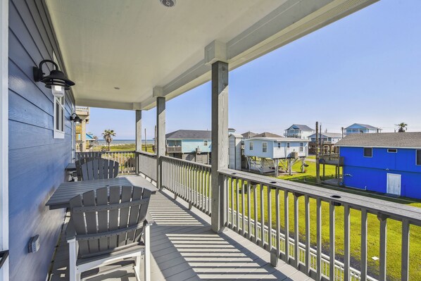 A covered porch with a table and chairs, overlooking a residential area with houses and a clear sky. - Sandy Cheeks Surfside by Ryson Vacation Rentals (Freeport)