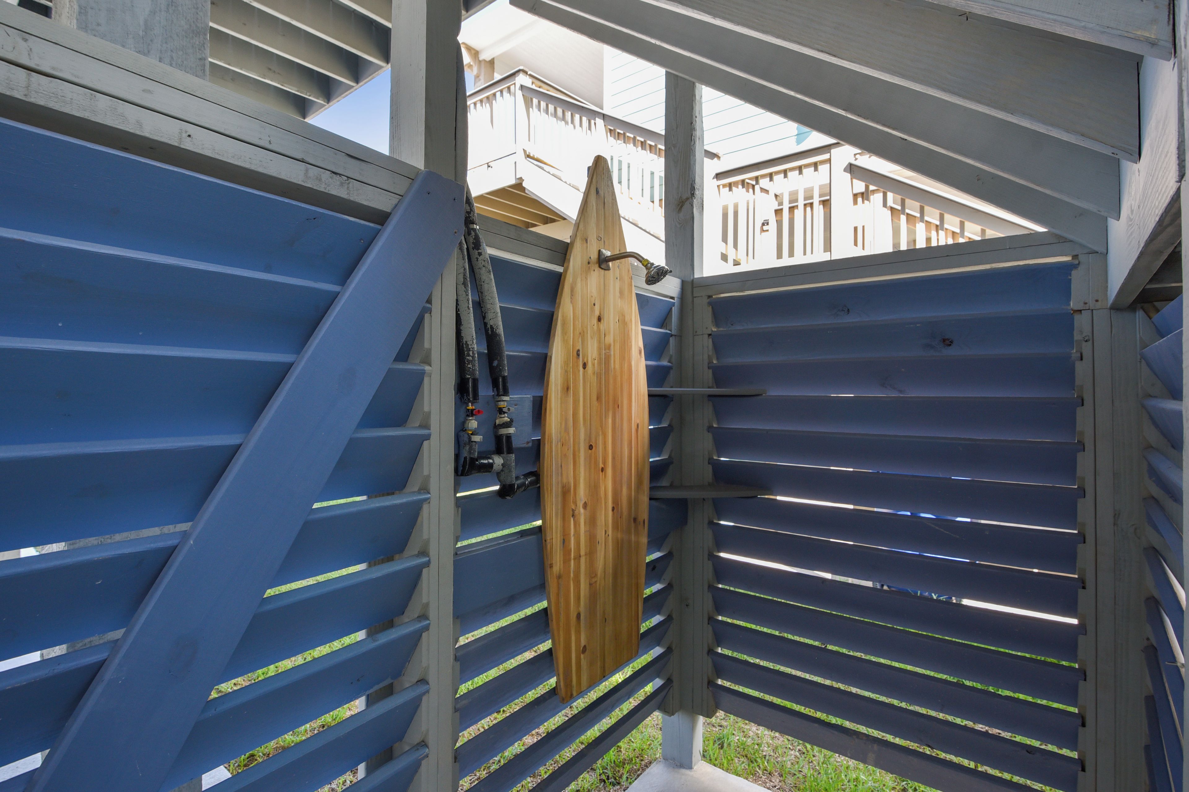 Ein Holzsurfbrett, das an einer blauen Metallkonstruktion mit einer Treppe, die zu einer oberen Ebene führt, lehnt.