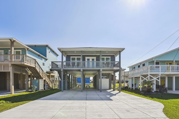 A row of beachfront condominiums with balconies, a central walkway, and a clear sky.
