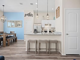 Una cocina moderna con armarios blancos, encimera de granito y una isla central con taburetes de bar.