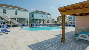 Ein Poolbereich mit blauen Liegestühlen, einer Holzpergola und einem Pool, umgeben von mehrstöckigen Gebäuden.