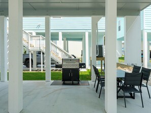 A covered outdoor patio with a grill, chairs, and a view of a house with a staircase. - Sandy Bottoms by Miss Kitty’s (Rockport)