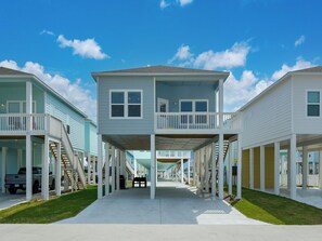 Fileira de casas de praia com dois andares, varandas, galeria coberta e céu azul límpido.