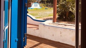 An open door leading to an outdoor patio area with a pergola, palm trees, and a blue sign. - Omontinho - 4-bed House With Pool in Melides (Grandola)