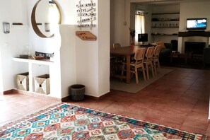 A spacious living area with a dining table, chairs, a TV, and a patterned rug.