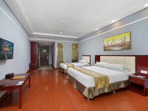 A hotel room with two beds, a wooden floor, a painting on the wall, and a desk with a chair.