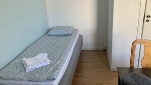 A small, single-bed room with a patterned bedspread, a folded towel, and a wooden chair. - Apartment in Hagersten Stockholm (Hägersten)