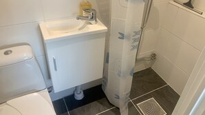 A bathroom with a white sink, toilet, and shower curtain with a leaf pattern. - Apartment in Hagersten Stockholm (Hägersten)
