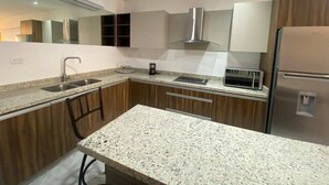 A modern kitchen with granite countertops, stainless steel appliances, and wooden cabinets. - Condos MDS7A ByTrvl2hm (Mazatlán)