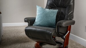 A black leather chair with a teal cushion, positioned in a room with a carpeted floor and a gray wall. - Valley Views Apartment  (Happy Valley)