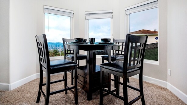 A dining area with a round table and four chairs, large windows with blinds, and a carpeted floor. - Valley Views Apartment  (Happy Valley)