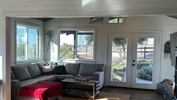A cozy living room with a sectional sofa, a coffee table, and a red throw blanket. There are large windows and a door leading to an outdoor area. - Templeton Vineyard Farmhouse in the Heart of Wine Country  (Templeton)