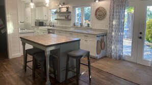 A modern kitchen with white cabinets, a large island with stools, pendant lighting, and a farmhouse sign. - Templeton Vineyard Farmhouse in the Heart of Wine Country  (Templeton)