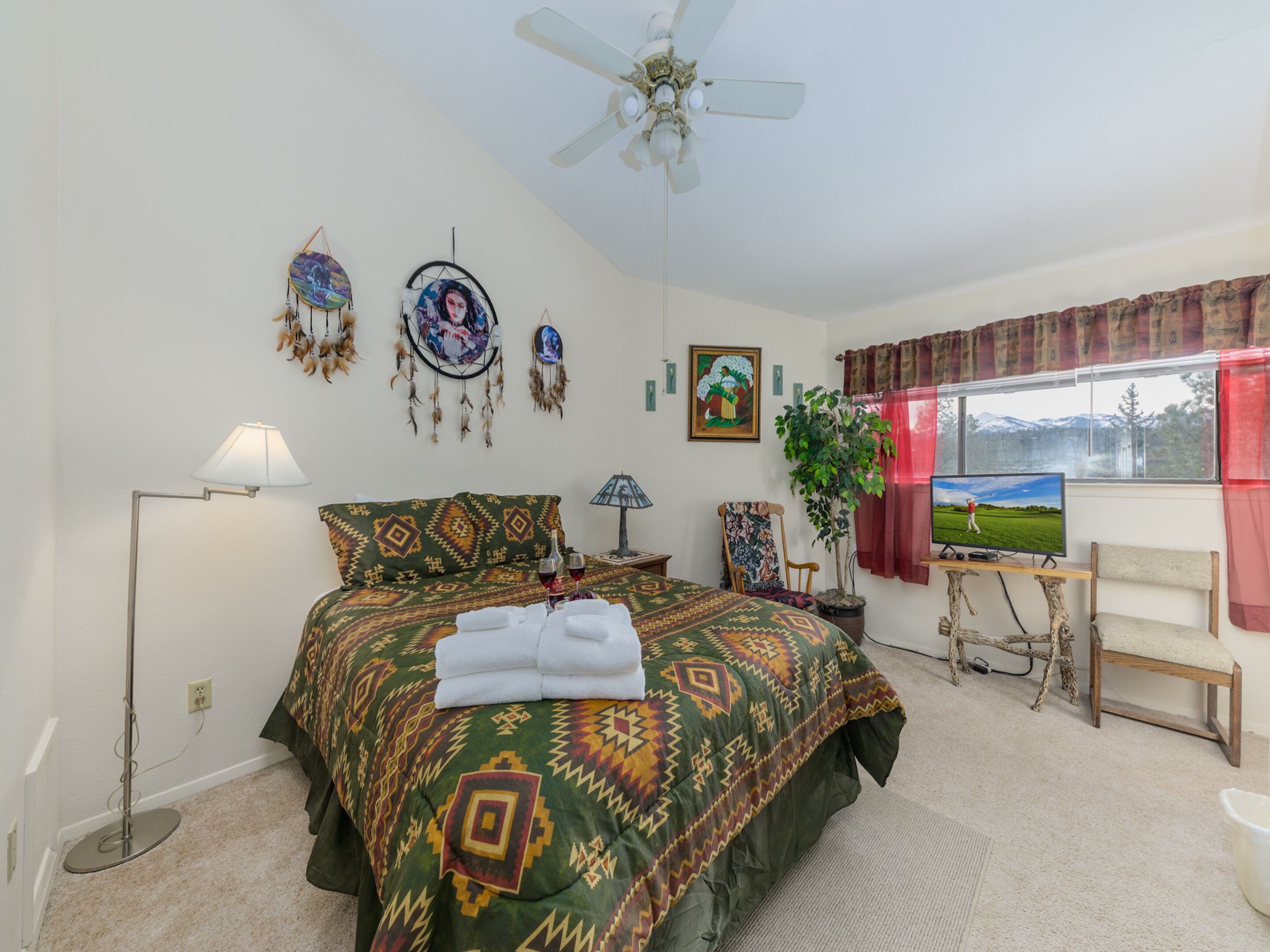 Ein Schlafzimmer mit Bett, Deckenventilator, Fernseher, Pflanze und Fenster mit Blick.