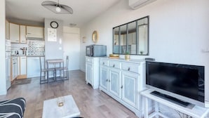 A modern living room with a flat-screen TV, a dining area with a table and chairs, and a kitchen with white cabinets and a tiled backsplash. - T2 600 m from the beach! Air-conditioned (Le Lavandou)
