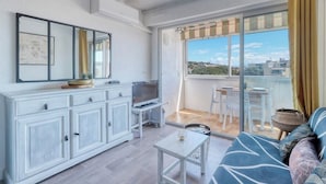 A modern living room with a sofa, a TV, a dining table, and a balcony with a view of the city. - T2 600 m from the beach! Air-conditioned (Le Lavandou)