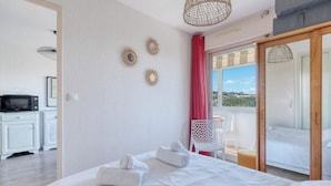 A hotel room with a bed, a desk with a microwave, a chair, and a view of the outside. - T2 600 m from the beach! Air-conditioned (Le Lavandou)