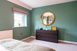 A bedroom with a bed, a dresser, a mirror, a window with blinds, and a radiator.