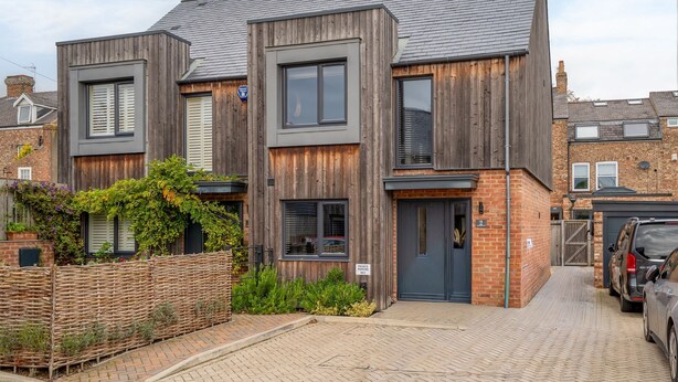Une maison moderne à deux étages, dotée d’une façade en briques et d’un revêtement en bois.