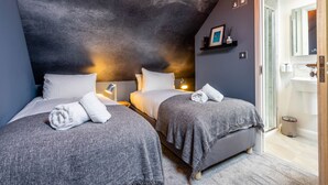 Une chambre d’hôtel avec deux lits, un plafond sombre et une salle de bain visible à travers une porte ouverte.