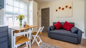 A modern living room with a grey sofa, red cushions, a wooden dining table, and a vase of flowers. - 44B Fishergate -  a couples retreat that sleeps 3 guests (York)