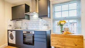 A modern kitchen with a built-in washer and oven, a wooden table with a vase of flowers, and a window with blinds. - 44B Fishergate -  a couples retreat that sleeps 3 guests (York)