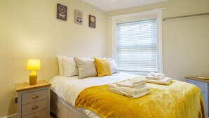 A neatly made bed with a yellow throw blanket, a bedside lamp, and a nightstand with drawers. - 44B Fishergate -  a couples retreat that sleeps 3 guests (York)
