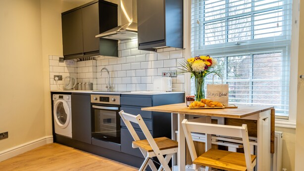 A compact kitchen with a built-in oven, a washing machine, and a dining area with a table and chairs. - 44B Fishergate -  a couples retreat that sleeps 3 guests (York)