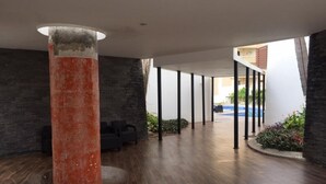 Amplo espaço interno com piso de madeira, um grande pilar e vista para uma piscina ao ar livre.