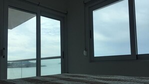 Quarto com uma cama grande, vista para um corpo d'água pela janela e uma varanda com guarda-corpo.