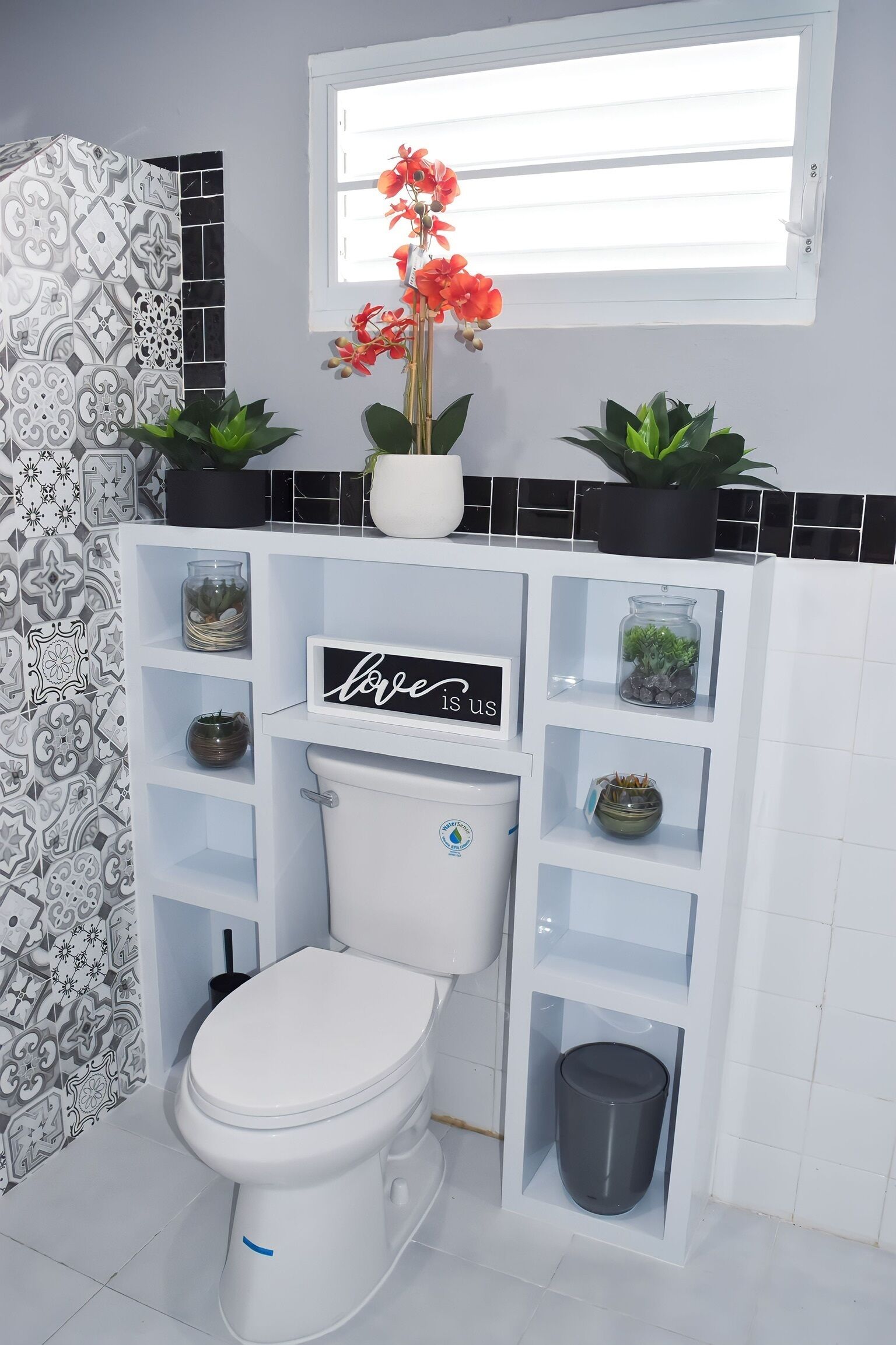 Ein modernes Badezimmer mit Toilette, Regalen mit Dekoration und einem Fenster mit Pflanzen.