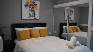 Habitación de hotel con cama, espejo y un cuadro de un perro usando un tocado colorido.