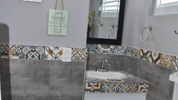 Un baño con tocador blanco, espejo y salpicadero de azulejos.