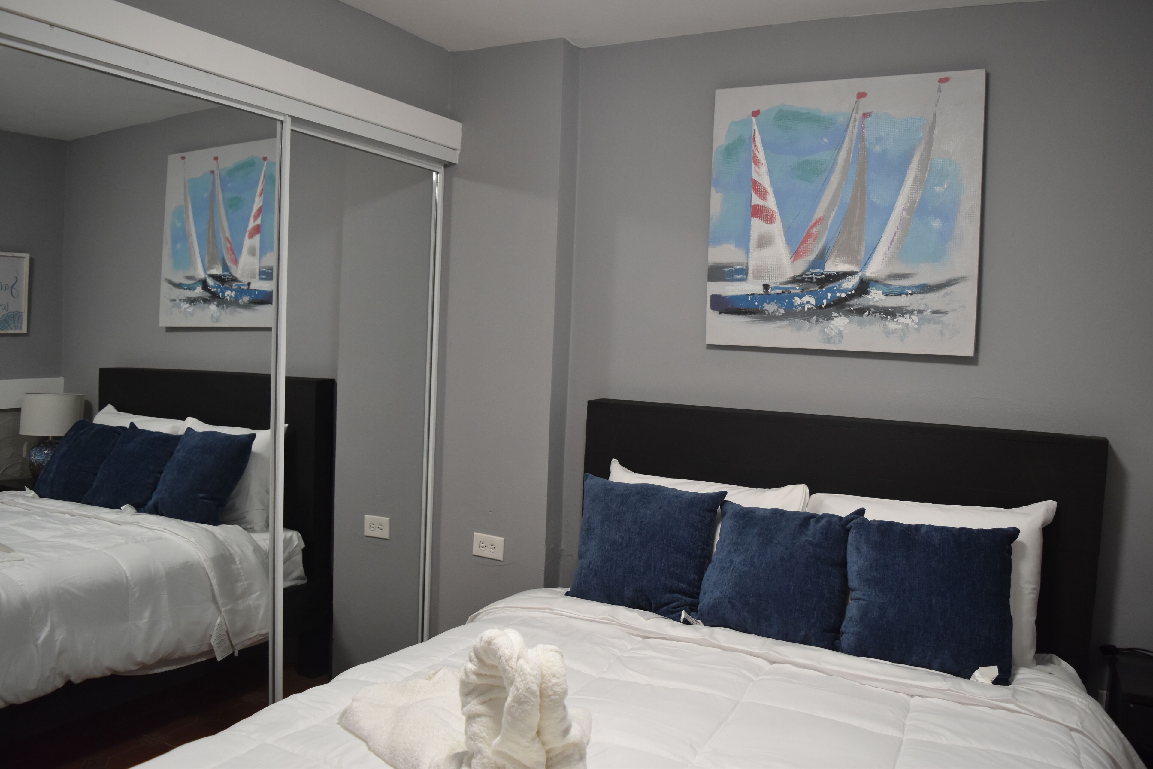 A hotel room with a large bed, a mirror, and a painting of sailboats on the wall.