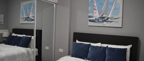 A hotel room with a large bed, a mirror, and a painting of sailboats on the wall.