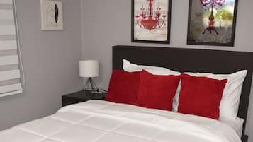 A neatly made bed with white bedding and red pillows, a bedside lamp, and two wall art pieces above it.
