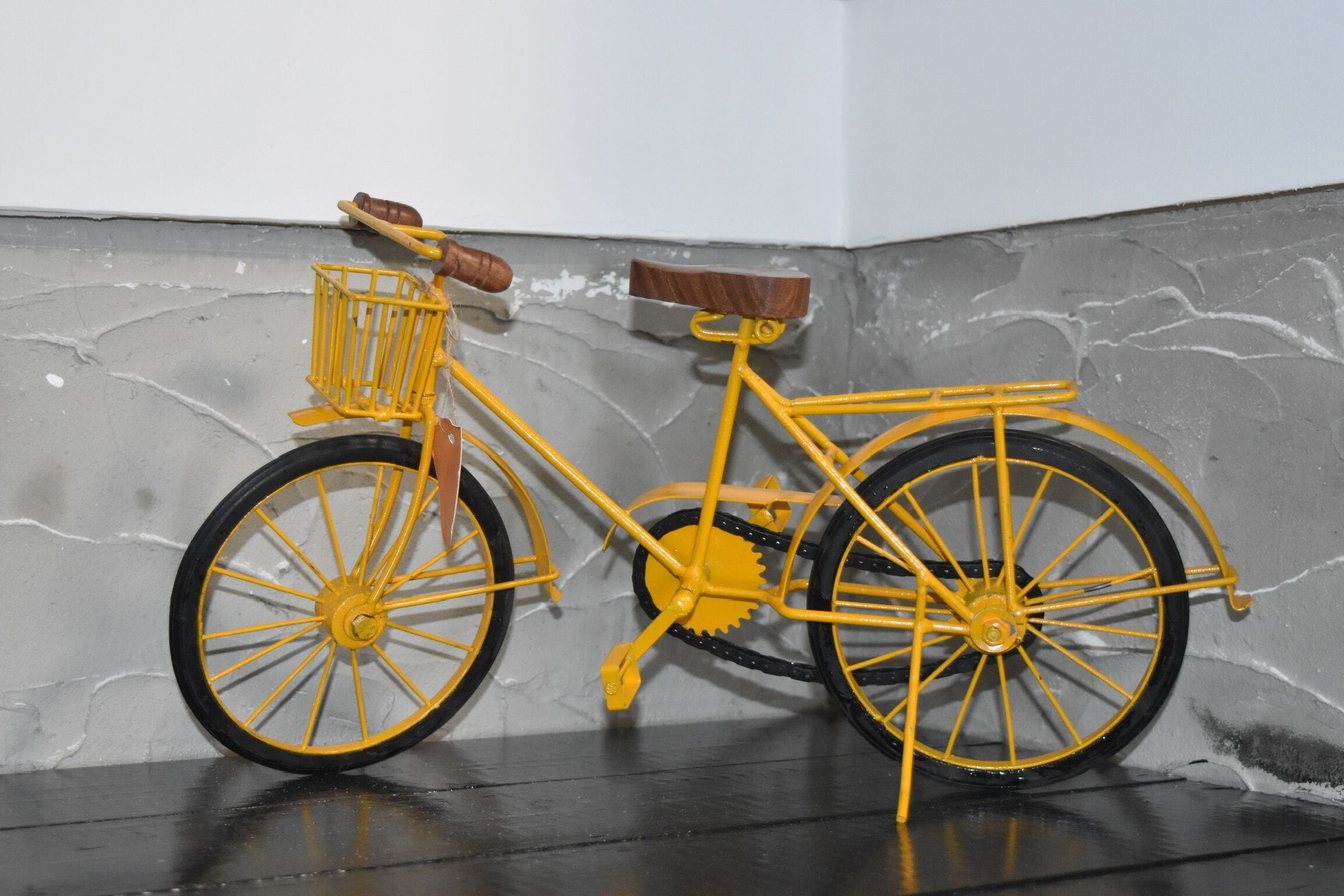Uma bicicleta amarela com cesto e selim encostada a uma parede texturizada.
