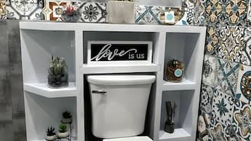 Un baño moderno con inodoro, estantes con plantas, un letrero decorativo y baldosas estampadas.