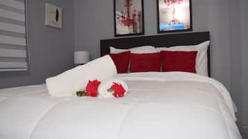 A neatly made bed with white and red bedding, a rolled towel, and a bouquet of red flowers.