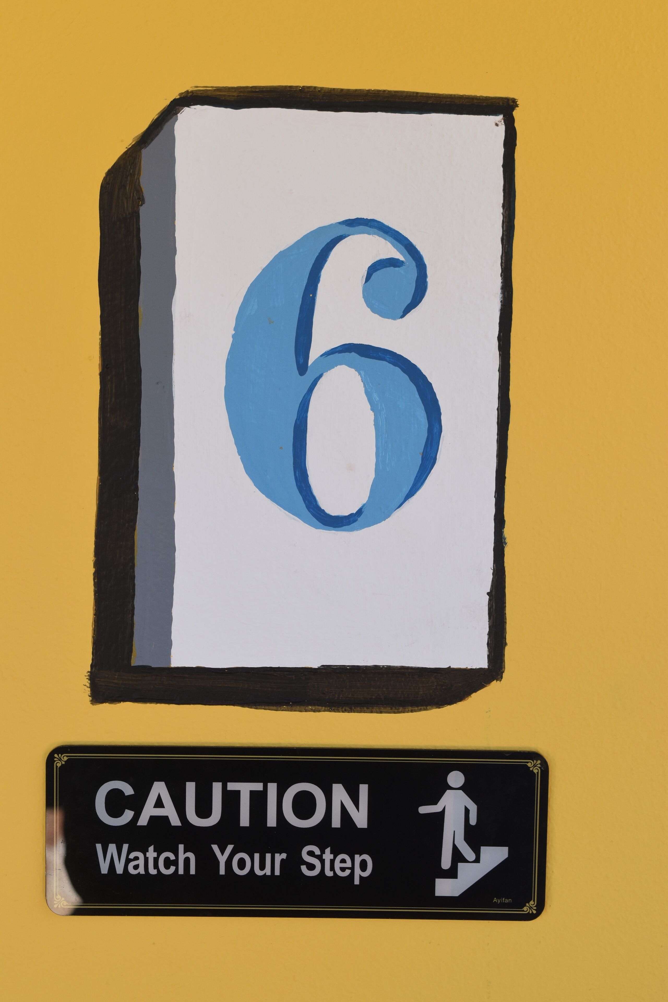 A sign with the number 6 and a caution sign below it that says "Watch Your Step".