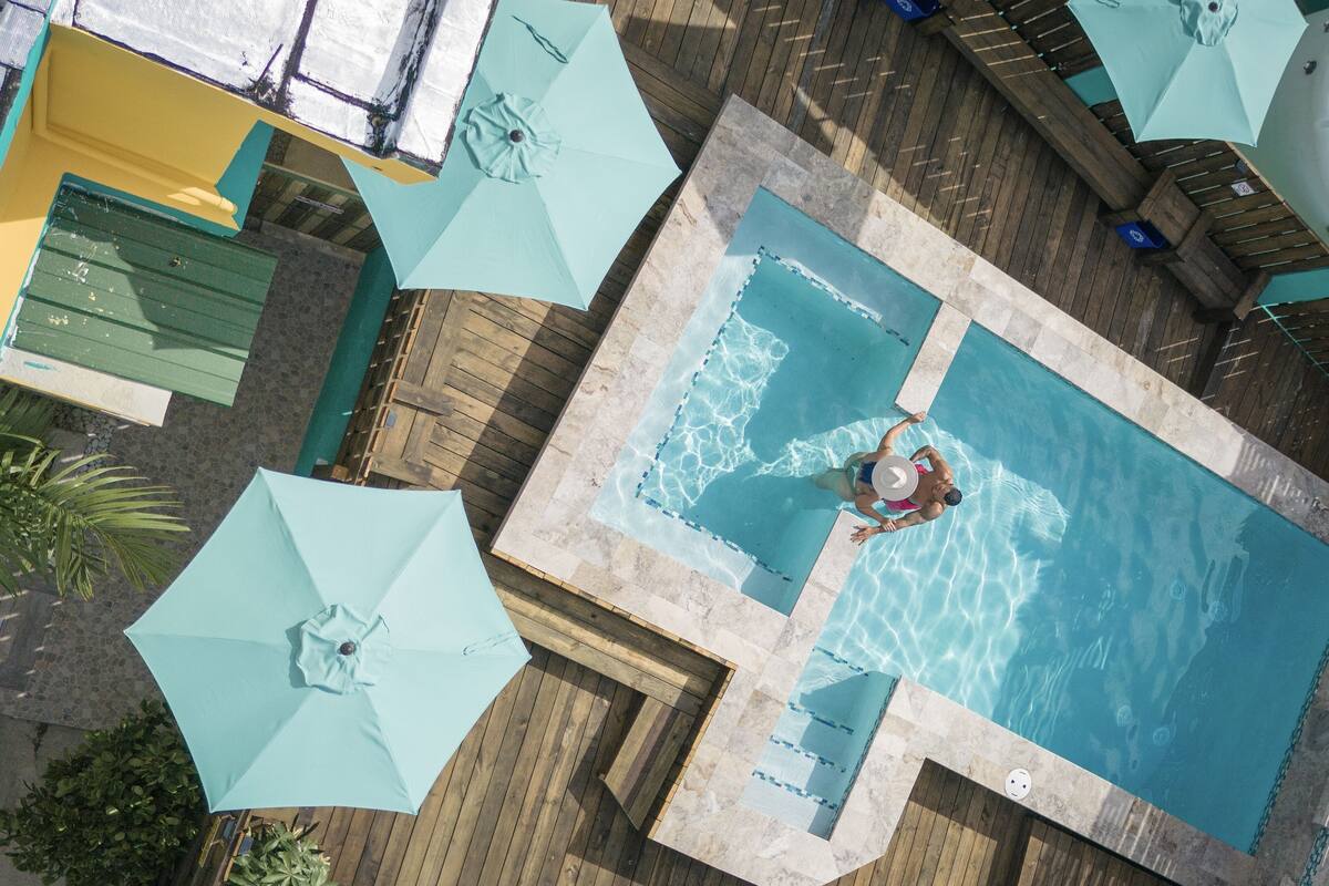 An aerial view of a swimming pool area with multiple umbrellas and lounge chairs.
