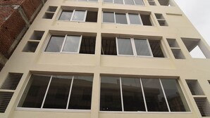 A multi-story building with a beige facade, large windows, and a brick wall on the left. - OYO 13310 Noida Suites (Noida)