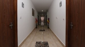 A hallway with wooden doors, a marble floor, and wall-mounted light fixtures. - OYO 13310 Noida Suites (Noida)