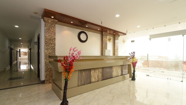 A reception desk with a clock, marble flooring, and two vases with flowers. - OYO 13310 Noida Suites (Noida)
